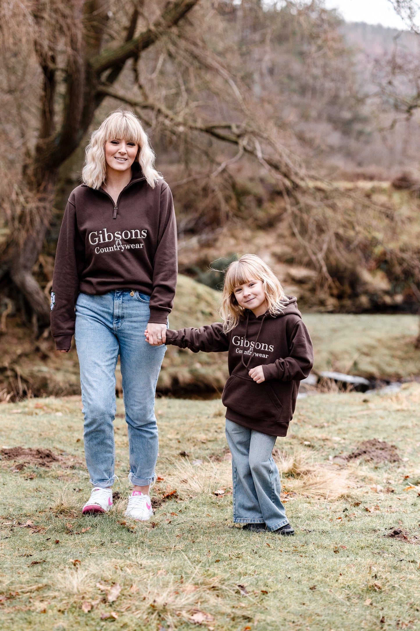Two people wearing brown 'Gibsons Countrywear' sweatshirts standing outdoors in a natural setting.