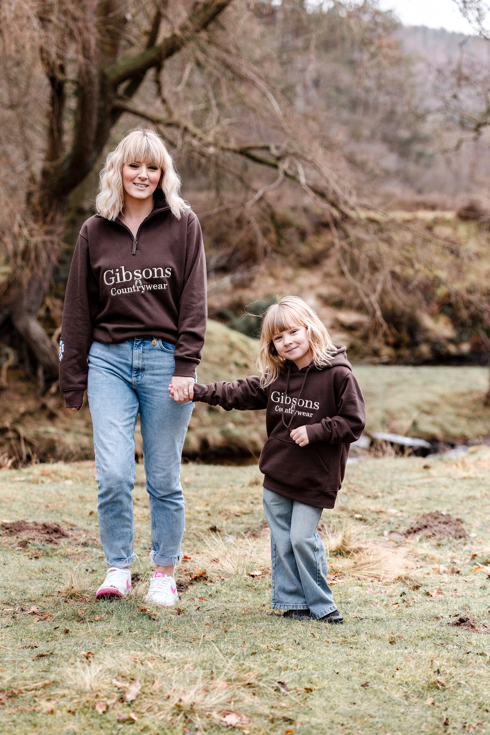Two people wearing brown 'Gibsons Countrywear' sweatshirts standing outdoors in a natural setting.