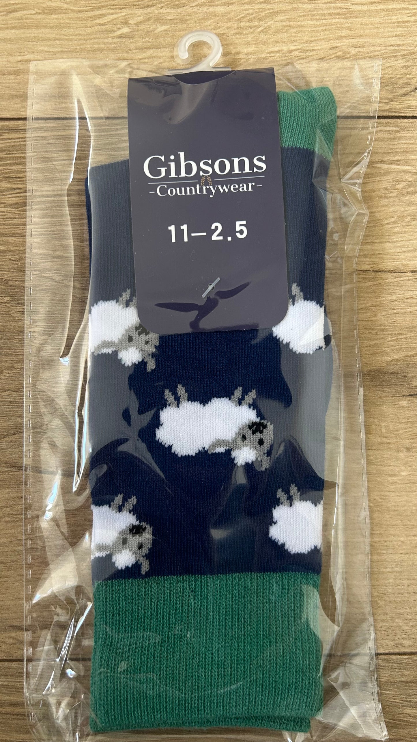 Packaged socks with a design of sheep and text 'Gibsons Countrywear' on a wooden surface.