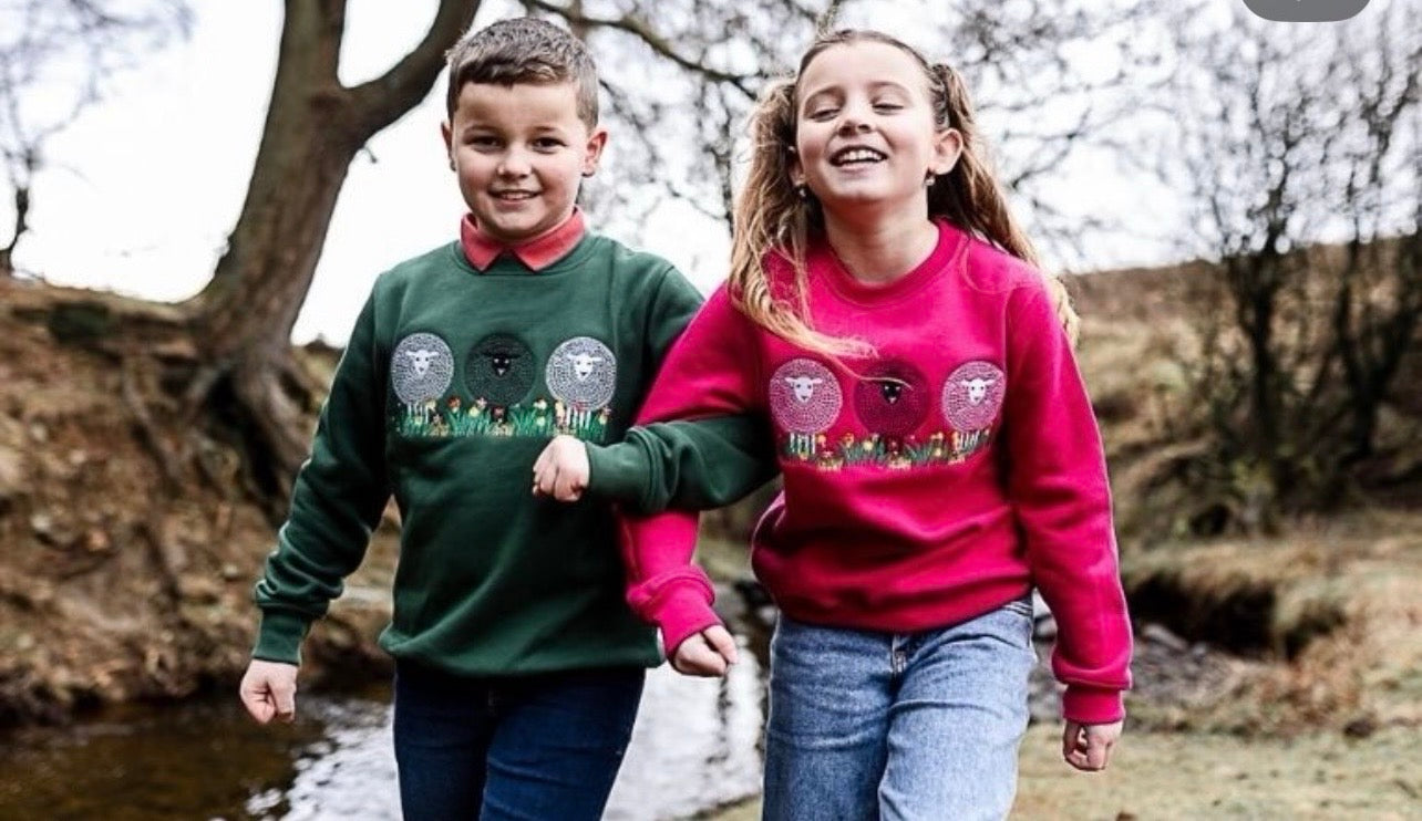 Two children wearing matching sweatshirts with a sheep design outdoors.