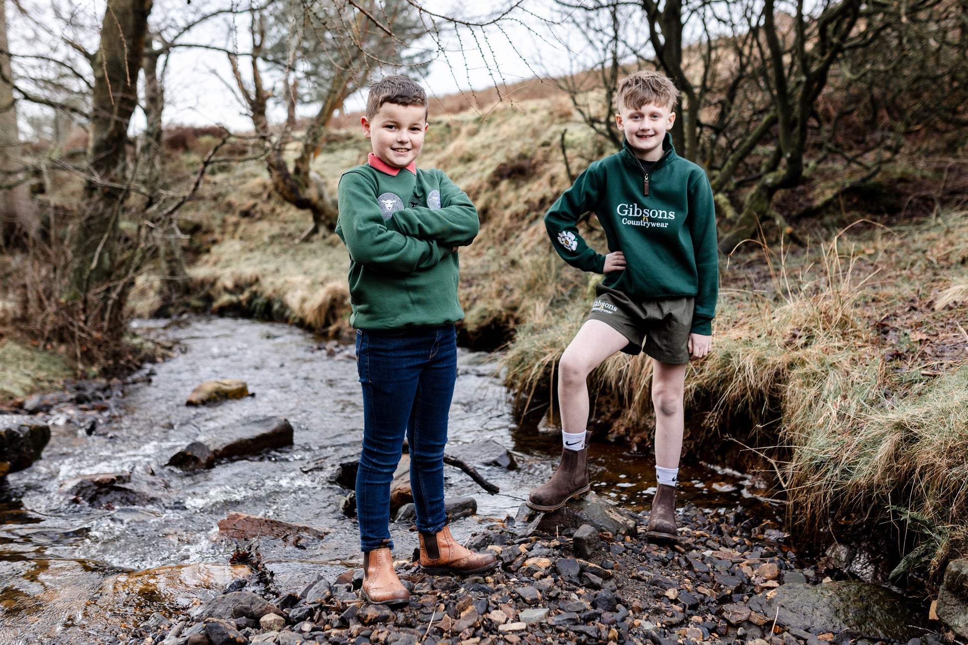 Two boys in green sweatshirts standing by a stream in a natural setting