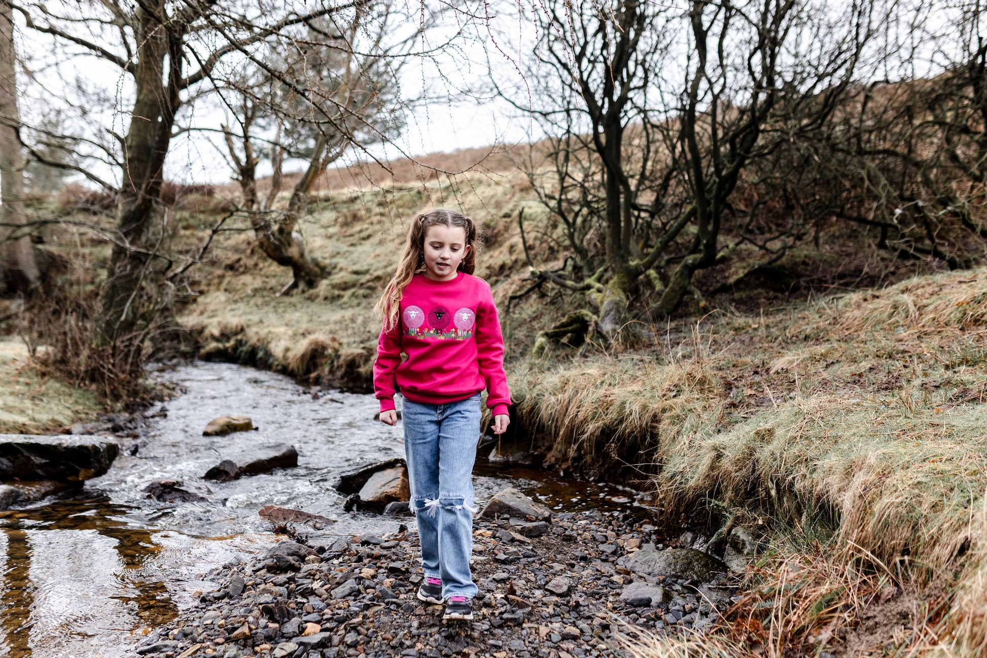 Young girl in a pink sweatshirt standing by a stream in a natural setting