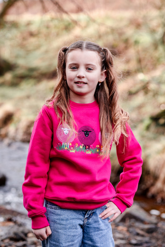 Young girl wearing a pink sweatshirt with a graphic design, standing outdoors near a stream.