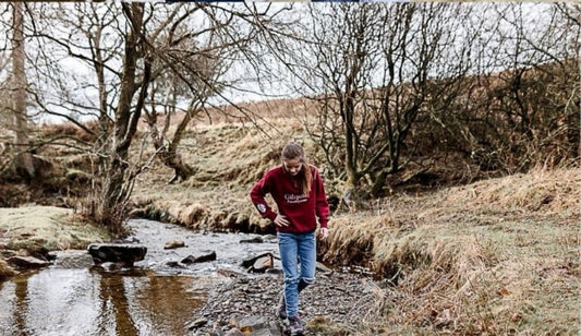 Person walking through a stream in a natural landscape with bare trees wearing Gibsons Country Wear