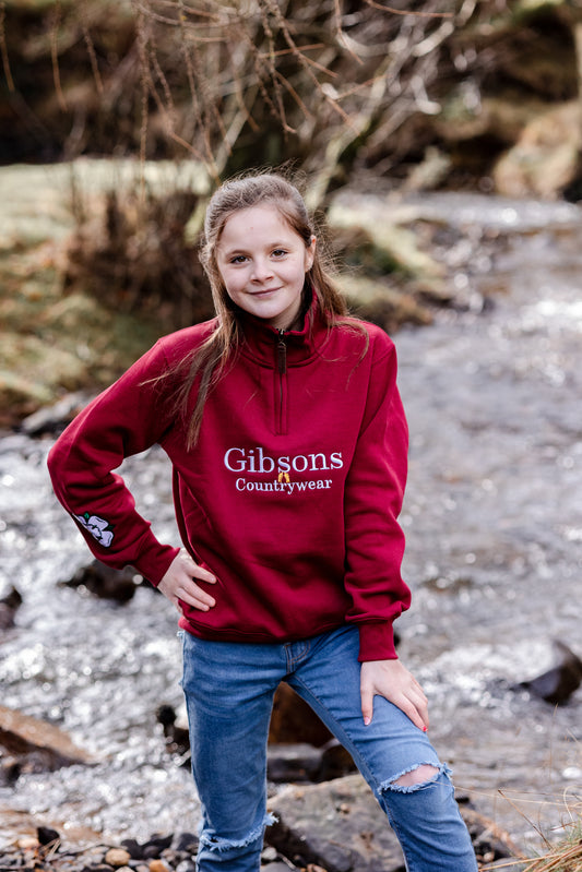 Person wearing a red 'Gibsons Countrywear' sweatshirt standing by a stream.