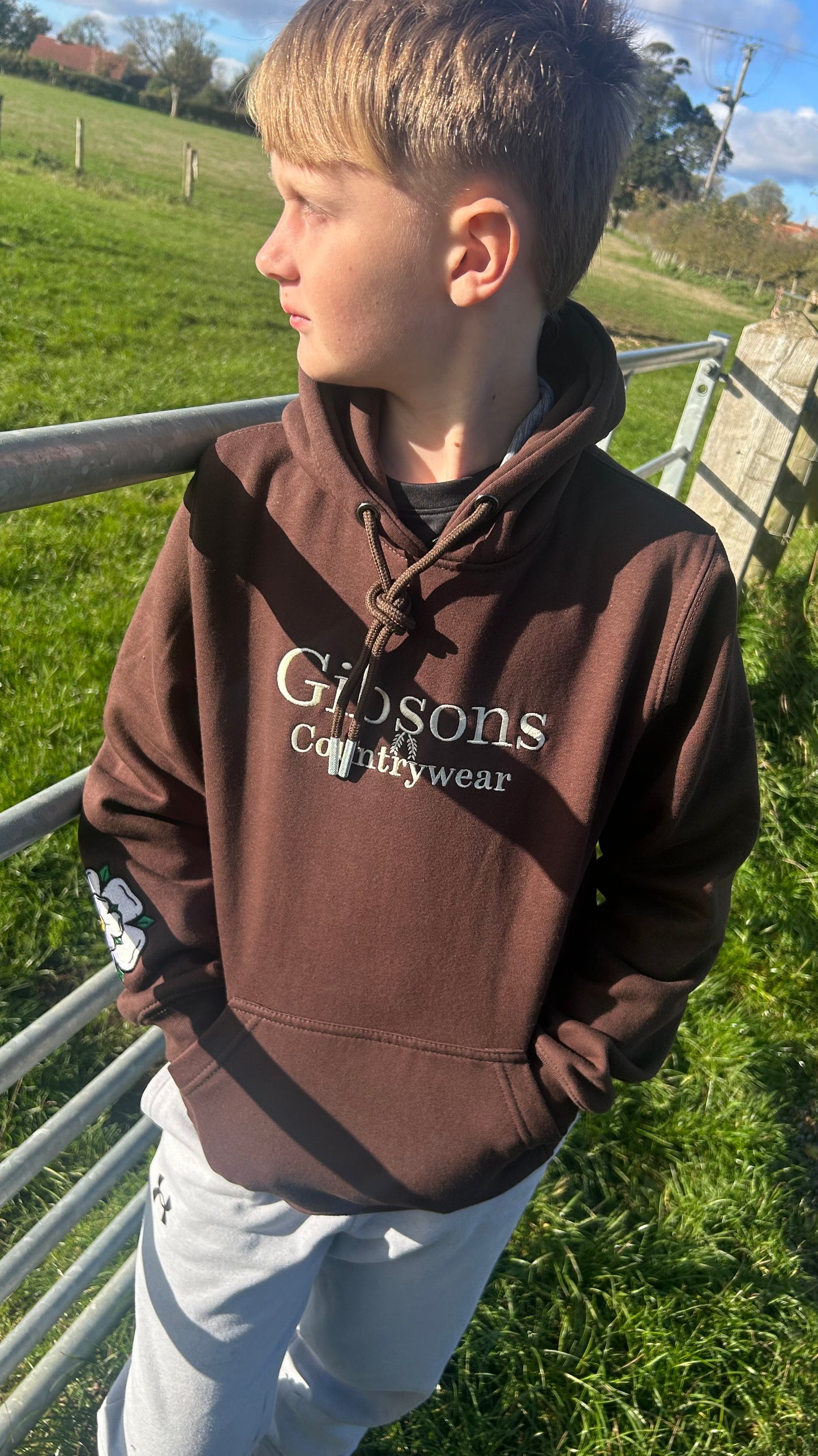 Child wearing a brown hoodie with 'Gibsons Countrywear' logo outdoors.