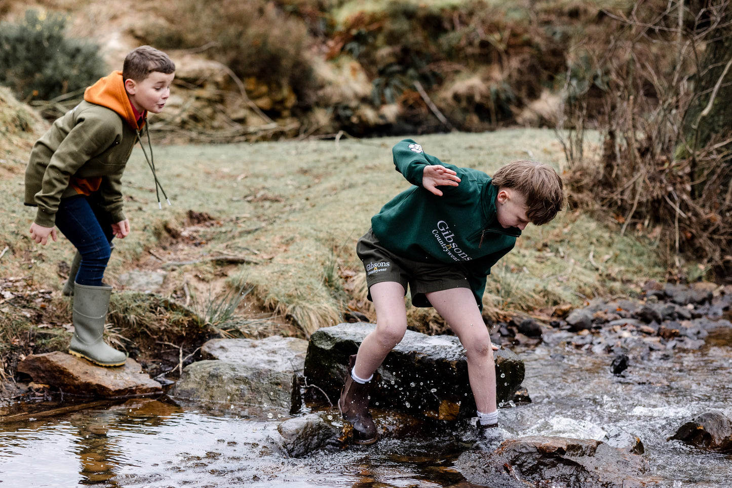 Two children playing in a stream with rocks and water.